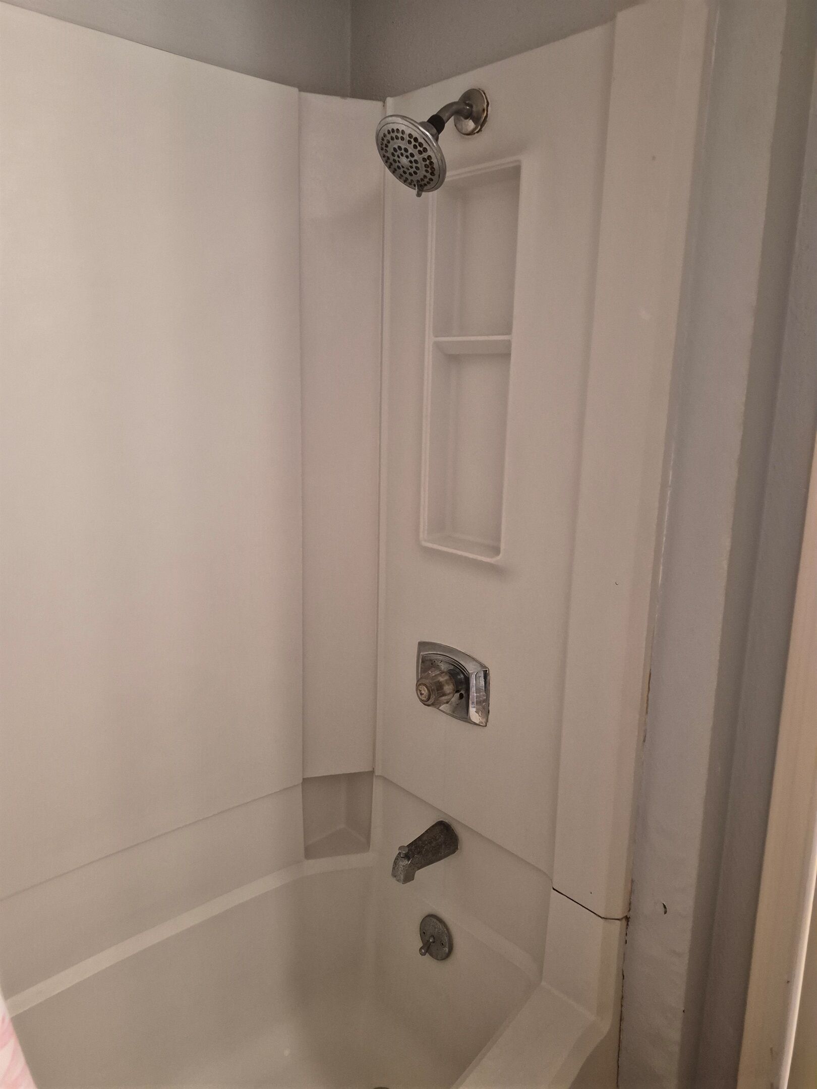 Eine Eckdusche mit Handbrause, Bedienfeld an der Wand und einer kleinen Ablagefläche.