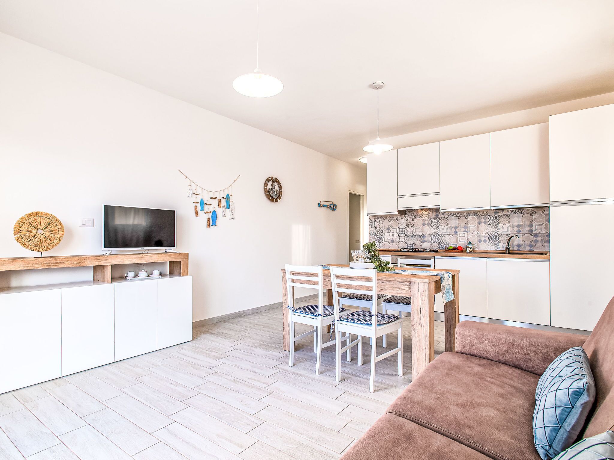 A modern kitchen with white cabinets, a dining area with a wooden table and chairs, and a living area with a brown sofa.