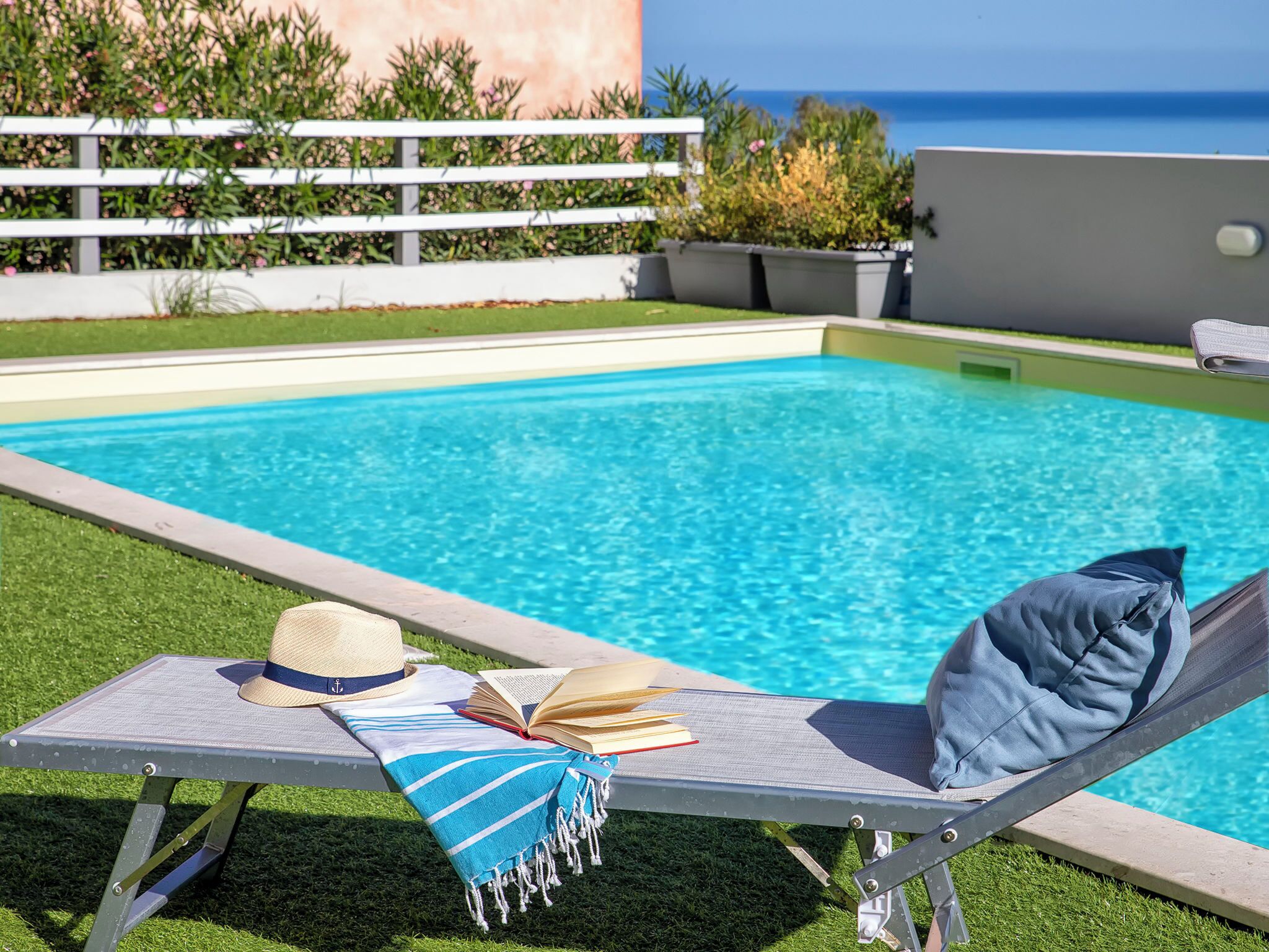 Eine Liege am Pool mit Hut, Buch und Handtuch.