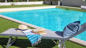 Eine Liege am Pool mit Hut, Buch und Handtuch.