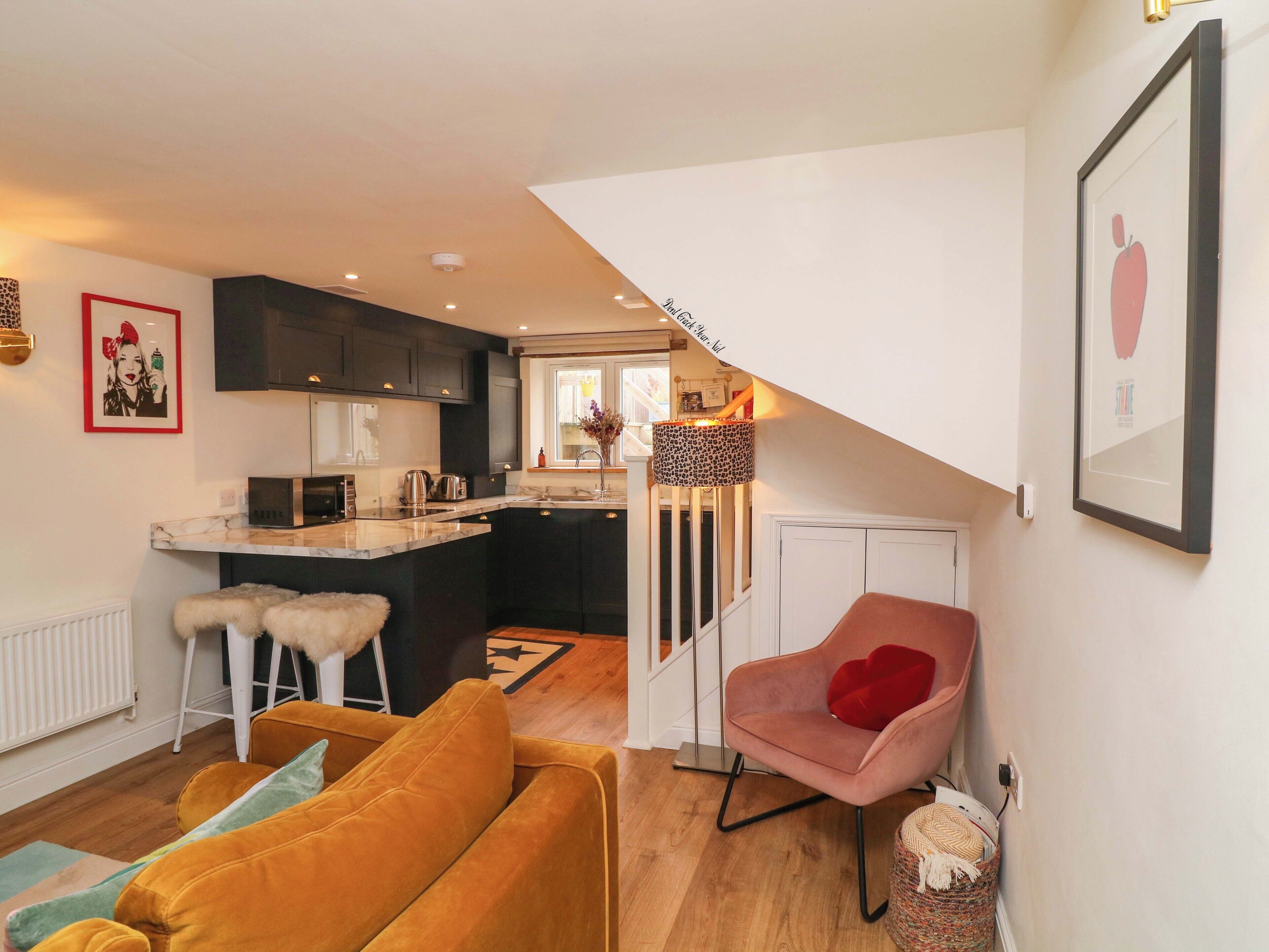 Ein modernes Wohnzimmer mit Sofa, Sessel, Küchenzeile mit Spüle und einer Treppe zu einer weiteren Ebene.