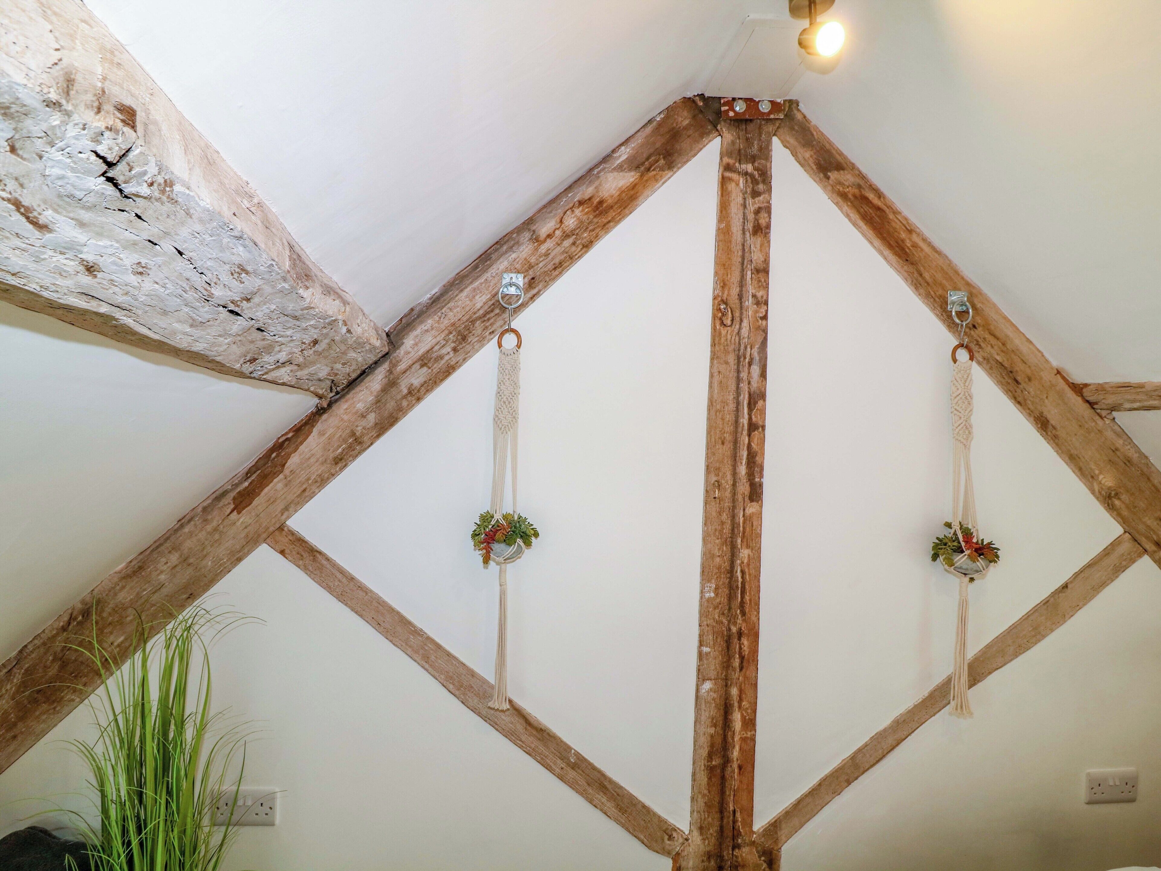 Ein Zimmer mit freiliegenden Holzbalken, einer weißen Decke und einem hängenden Wandbehang aus Makramee.