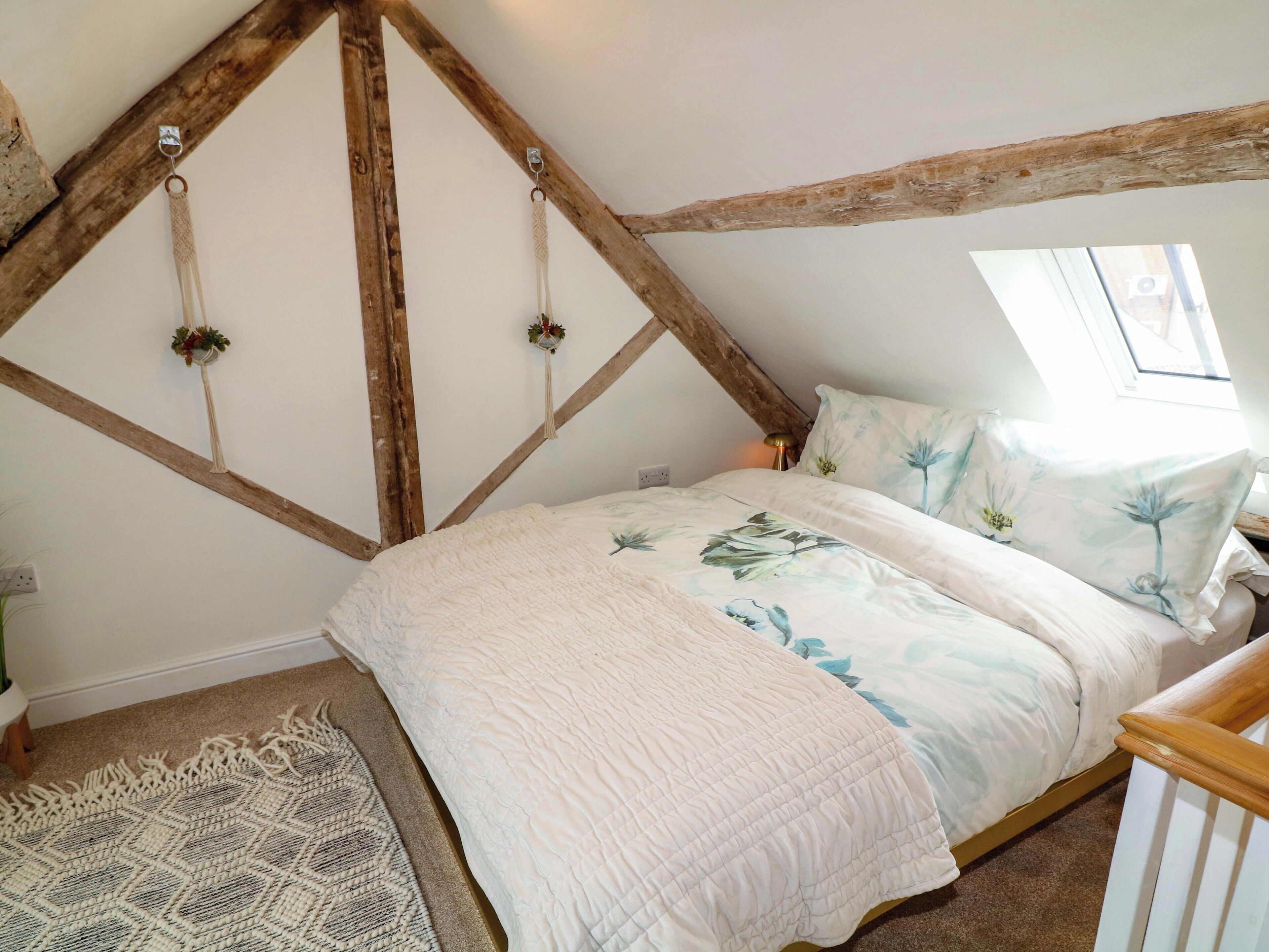 Un dormitorio con techo inclinado, una cama con ropa de cama floral, una alfombra tejida y un cabecero de madera.