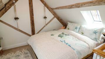 Un dormitorio con techo inclinado, una cama con ropa de cama floral, una alfombra tejida y un cabecero de madera.
