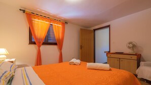 Una habitación de hotel con una cama, un armario de madera, un ventilador y una ventana con cortinas.
