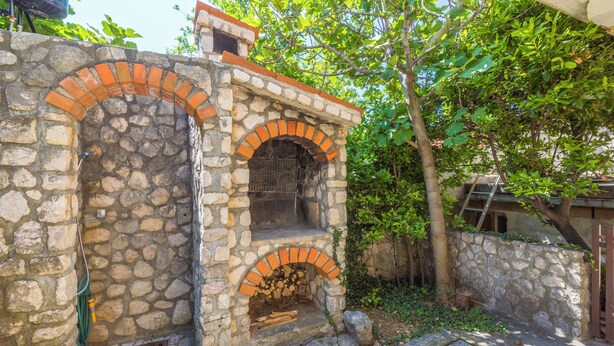 Estructura de horno de piedra al aire libre con chimenea, rodeada de vegetación y muros de piedra.