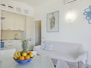 A modern kitchen with white cabinets, a dining table with a fruit bowl, a white sofa, and a wall-mounted map. - Anita Bados by Interhome (Pittulongu)