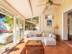 A living room with a sofa, a coffee table, a ceiling fan, a window with a view of the outside, and a wall-mounted picture. - Miramar by Interhome (La Londe Les Maures)