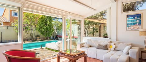 Amplia sala de estar con piscina, sillas rojas, una mesa de centro de madera y un ventilador de techo.