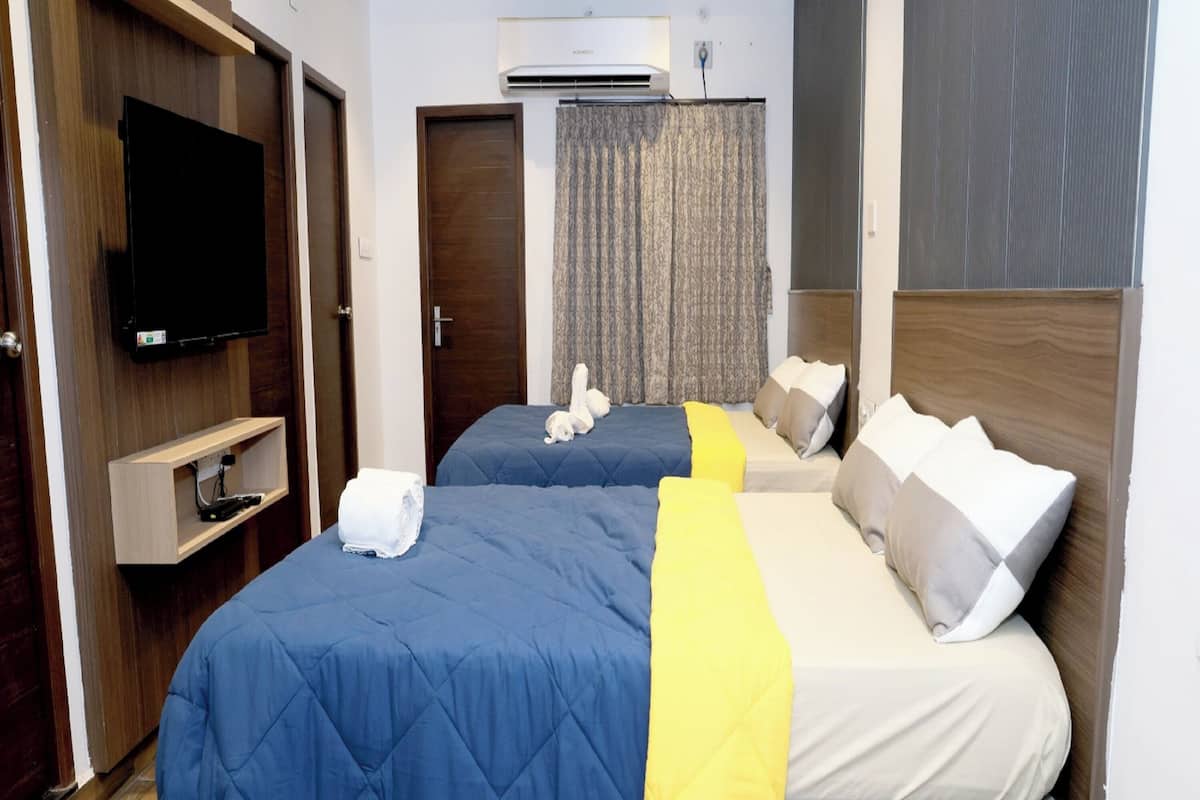 Habitación de hotel con dos camas, televisión, aire acondicionado y suelo de madera.