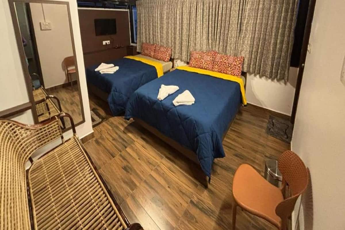 Una habitación con dos camas, ventilador de techo, televisión y ventana con cortinas.