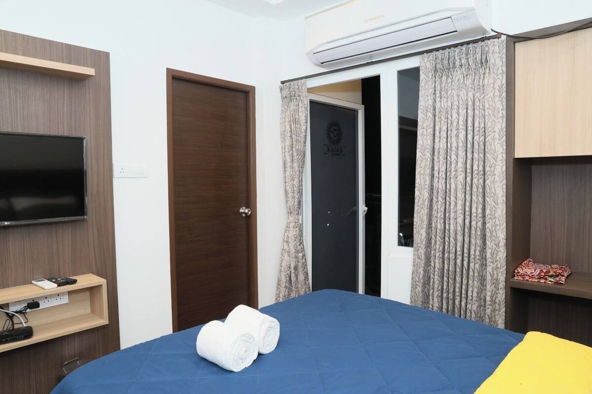 Una habitación de hotel con una cama, televisor, aire acondicionado, puerta y cortina.