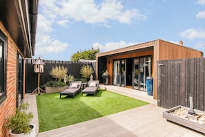 Een modern terras buiten met twee lounge fauteuils, een kleine tuin en een houten omheining.