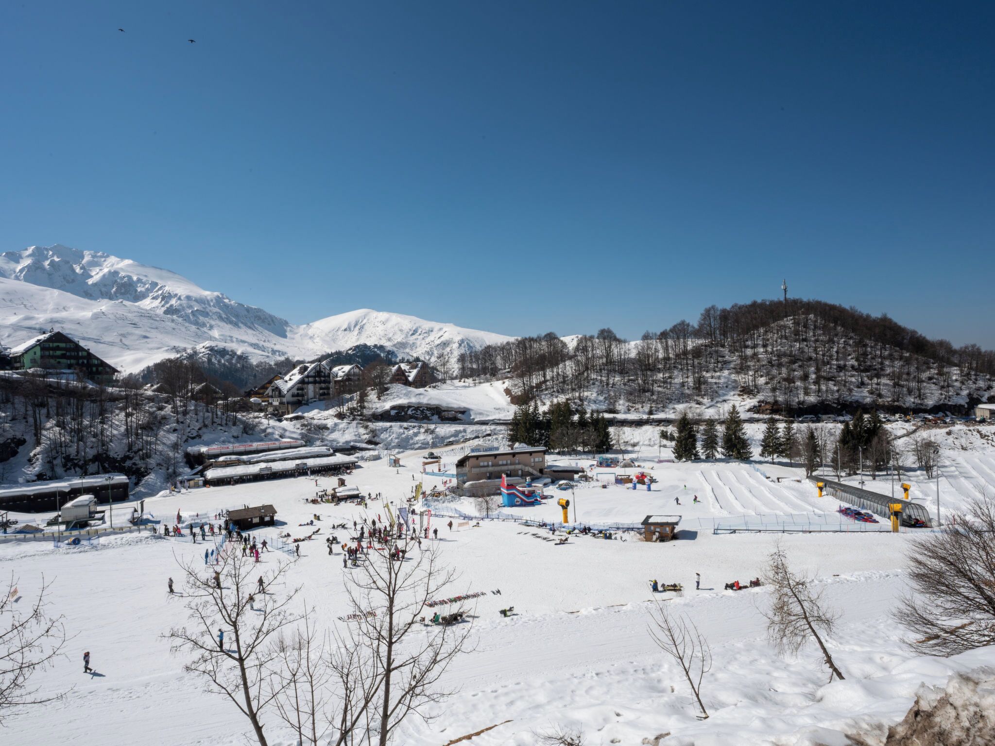 Een met sneeuw bedekte wintersportplaats met gebouwen, een skilift en bergen op de achtergrond.
