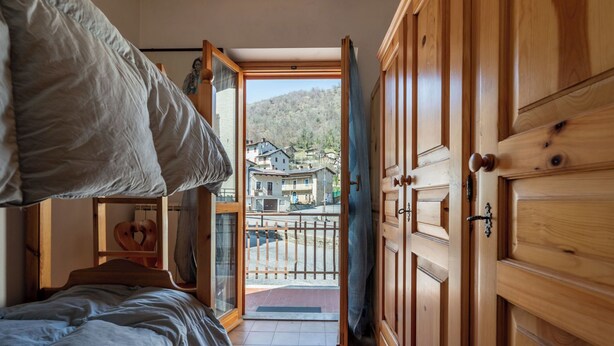 Una camera da letto con un letto, un armadio in legno e vista su un quartiere residenziale attraverso una porta aperta.