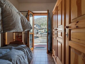 Quarto com cama, guarda-roupa de madeira e vista para uma área residencial através de uma porta aberta.