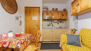 Una cucina compatta con pensili in legno, un tavolo da pranzo con tovaglia colorata e un divano giallo con copridivano decorato.