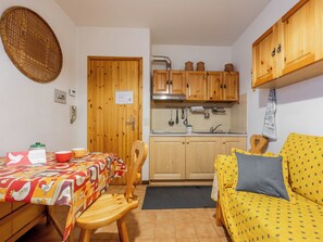A compact kitchen with wooden cabinets, a dining table with a colorful tablecloth, and a yellow sofa with a patterned cover. - Ai piedi del Monte by Interhome (Frabosa Sottana)