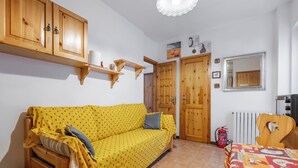 Una stanza con un divano giallo a fantasia, armadietti in legno, un termosifone e un letto con copripiumino colorato.