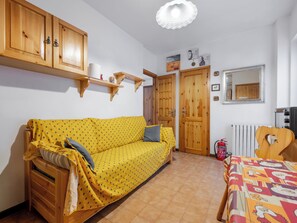 A room with a yellow patterned sofa, wooden cabinets, a radiator, and a bed with a colorful bedspread. - Ai piedi del Monte by Interhome (Frabosa Sottana)