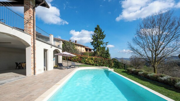 Une piscine à l’eau d’un bleu cristallin, entourée d’une terrasse aménagée avec des meubles d’extérieur et offrant une vue sur les montagnes.