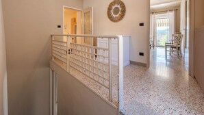 Un couloir avec une rambarde blanche, un luminaire au plafond, un élément décoratif mural et une vue sur un balcon extérieur.