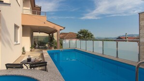 A swimming pool with a glass barrier, a covered patio, and a view of distant mountains. - Holiday Home Vele With Pool (Vrgorac)