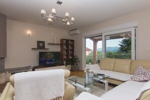 Ein Wohnzimmer mit Sofa, Glastisch, Fernseher und Bücherregal.