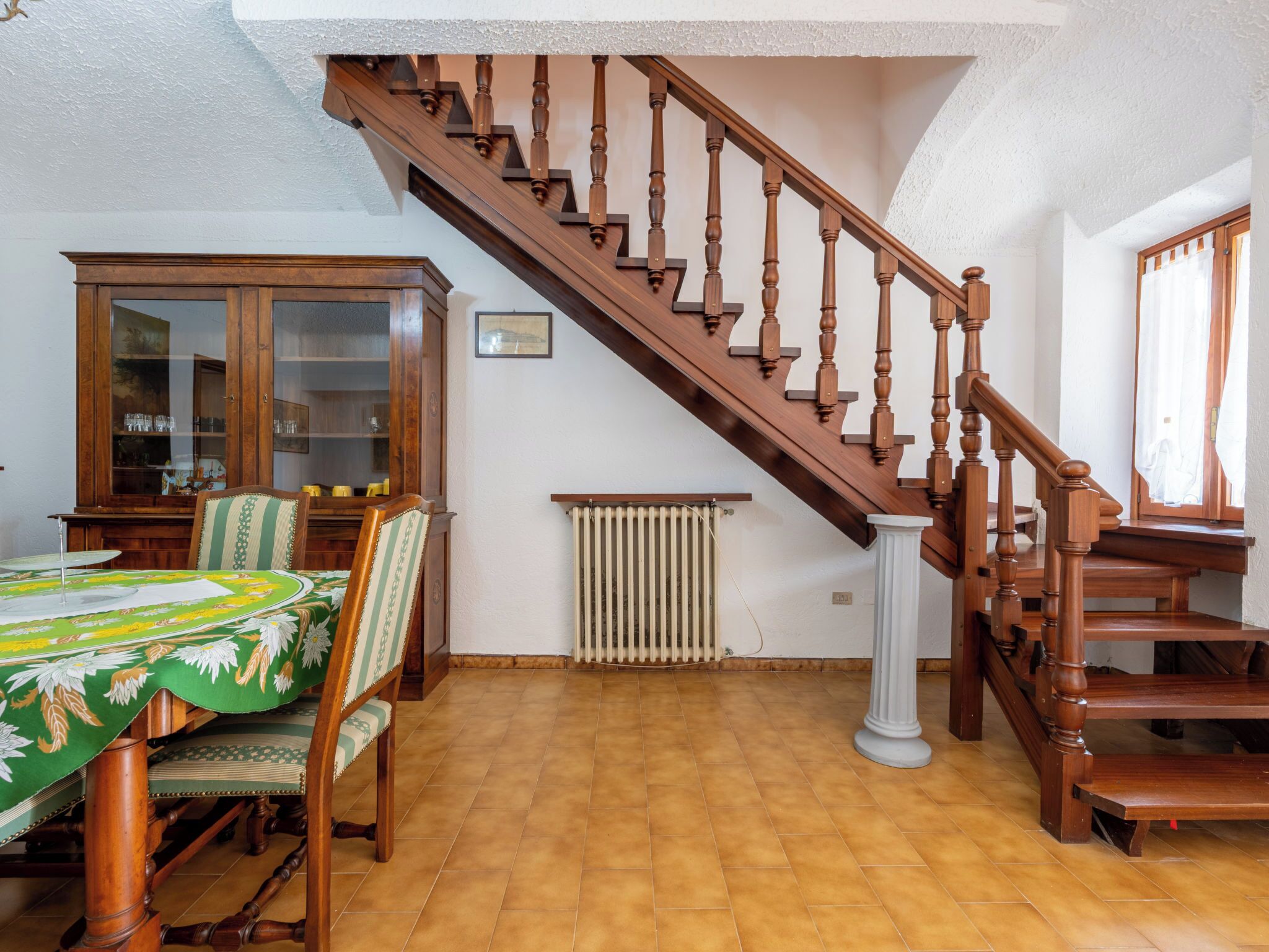 Un coin repas avec un escalier en bois, un radiateur et un meuble.
