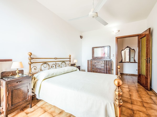 Un dormitorio con una cama, una mesita de noche, un aparador, un ventilador de techo y una puerta.
