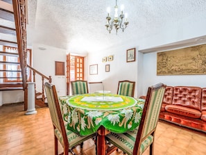 Un comedor con una mesa redonda, sillas, una araña, una escalera y un cuadro grande en la pared.