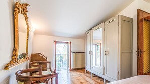 Ein Schlafzimmer mit einem Bett, einem Holzstuhl, einem großen Spiegel, einem Kleiderschrank und einer Heizung.