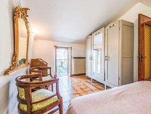 A bedroom with a bed, a wooden chair, a large mirror, a wardrobe, and a radiator.