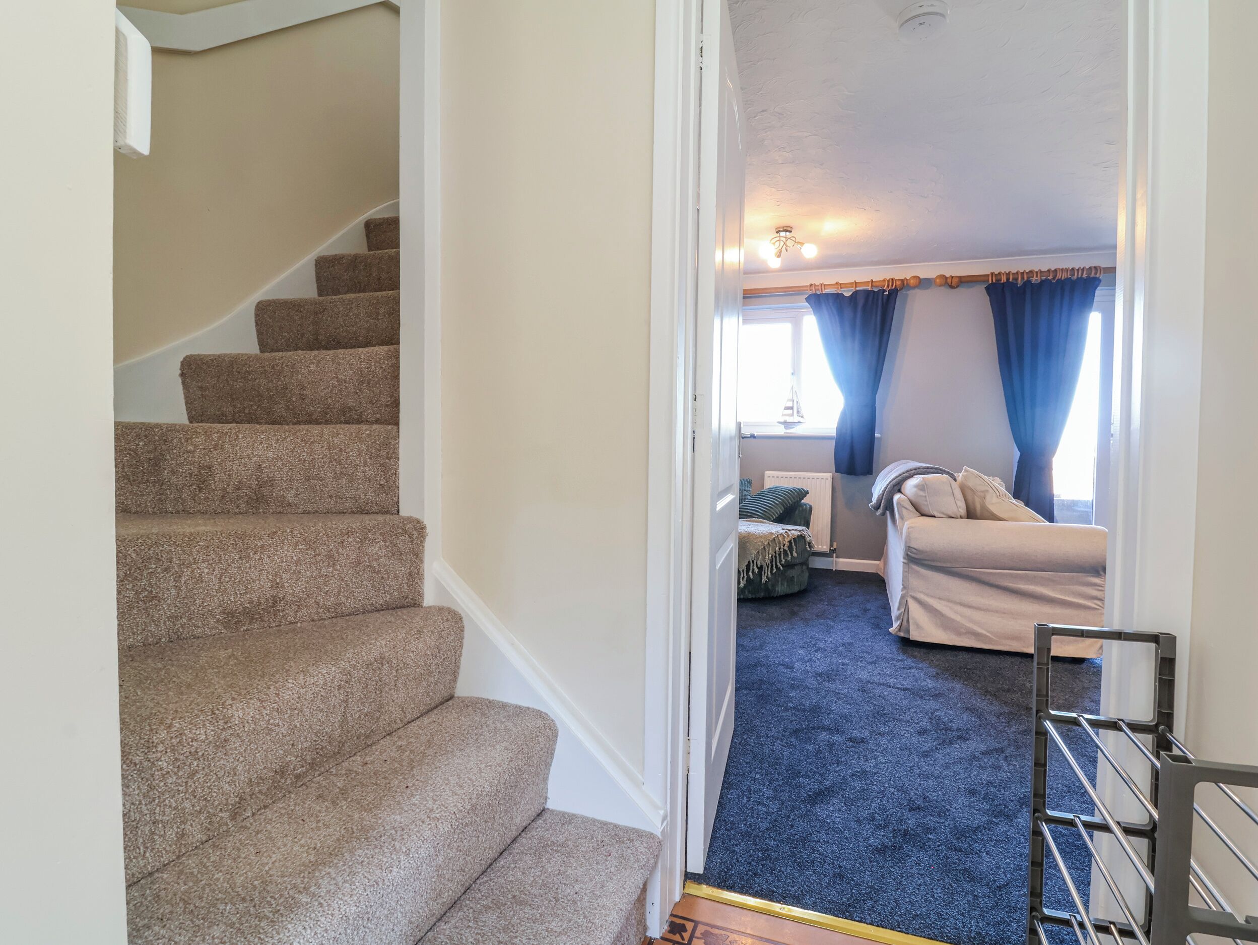 A carpeted staircase leading to a bedroom with a bed, a window with curtains, and a ceiling light fixture.