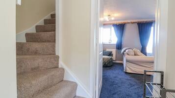 A carpeted staircase leading to a bedroom with a bed, a window with curtains, and a ceiling light fixture.