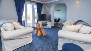 A living room with two sofas, a glass coffee table, a TV, and a dining area with a chair and table. - Sea Spray (Bideford)