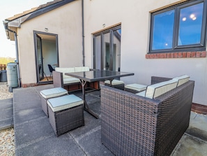 Un patio con una mesa de vidrio, mobiliario de mimbre y vista de la casa.
