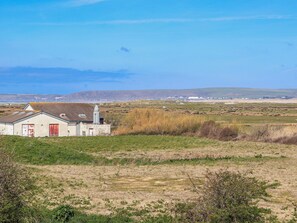 A rural landscape with a small white building featuring a red door and a chimney. - Sea Spray (Bideford)