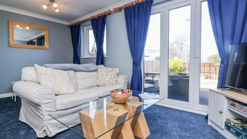A living room with a sofa, a glass coffee table, a television, and a sliding glass door leading to an outdoor area.