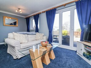 A living room with a sofa, a glass coffee table, a television, and a sliding glass door leading to an outdoor area.