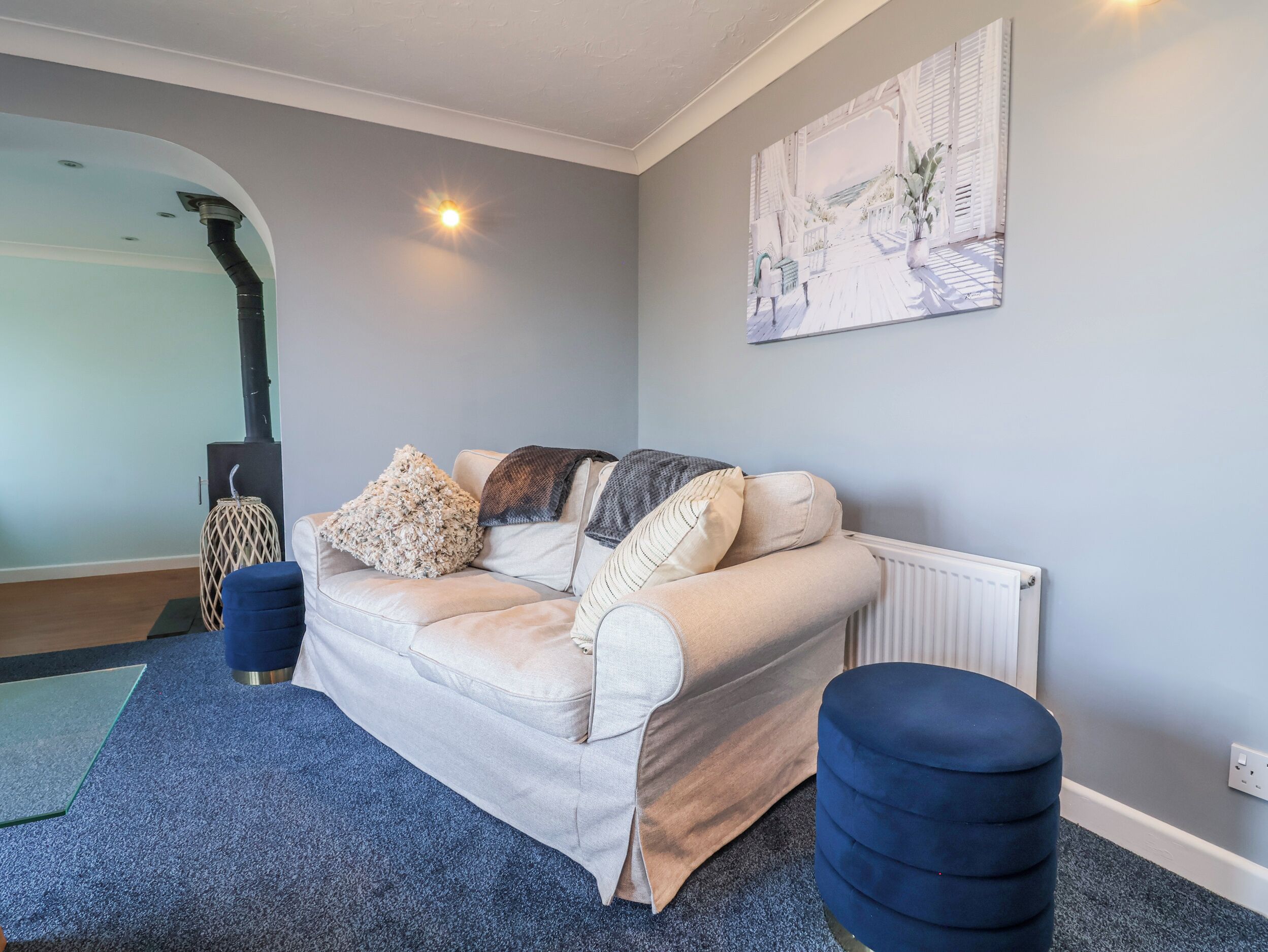 Een woonkamer met een bank, een voetenbankje en een schilderij aan de muur.