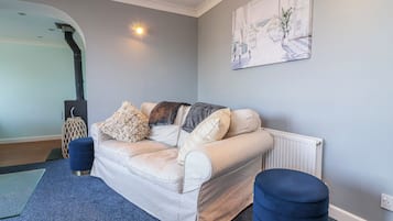 Een woonkamer met een bank, een voetenbankje en een schilderij aan de muur.