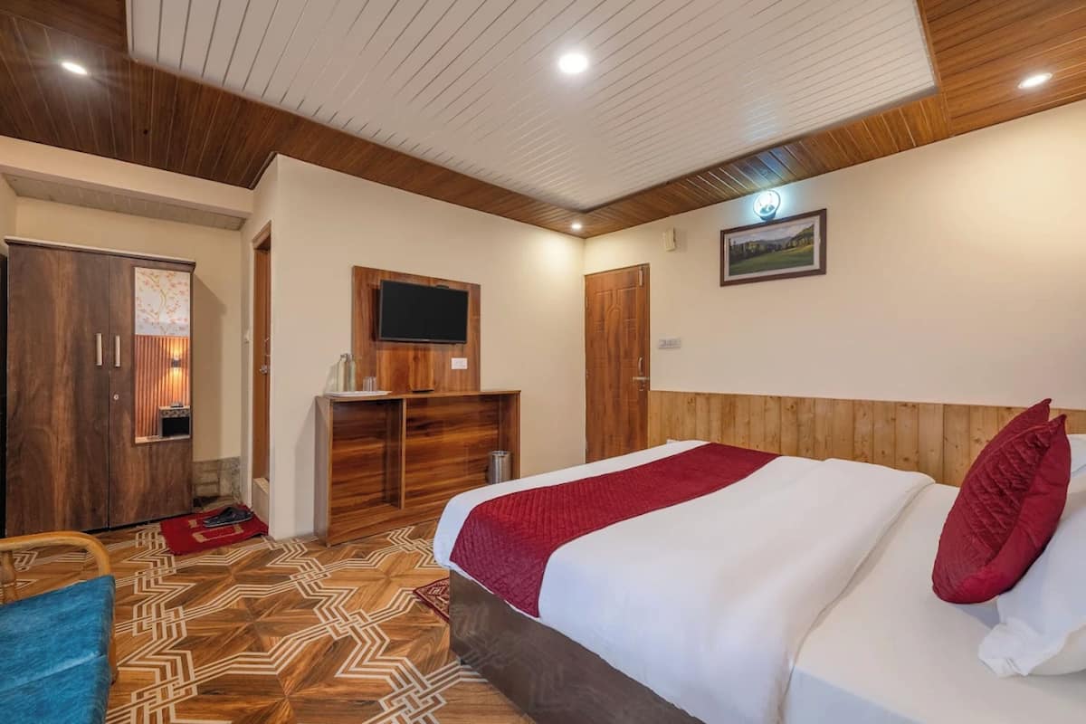 A hotel room with a bed, wooden wardrobe, television, and a patterned floor.