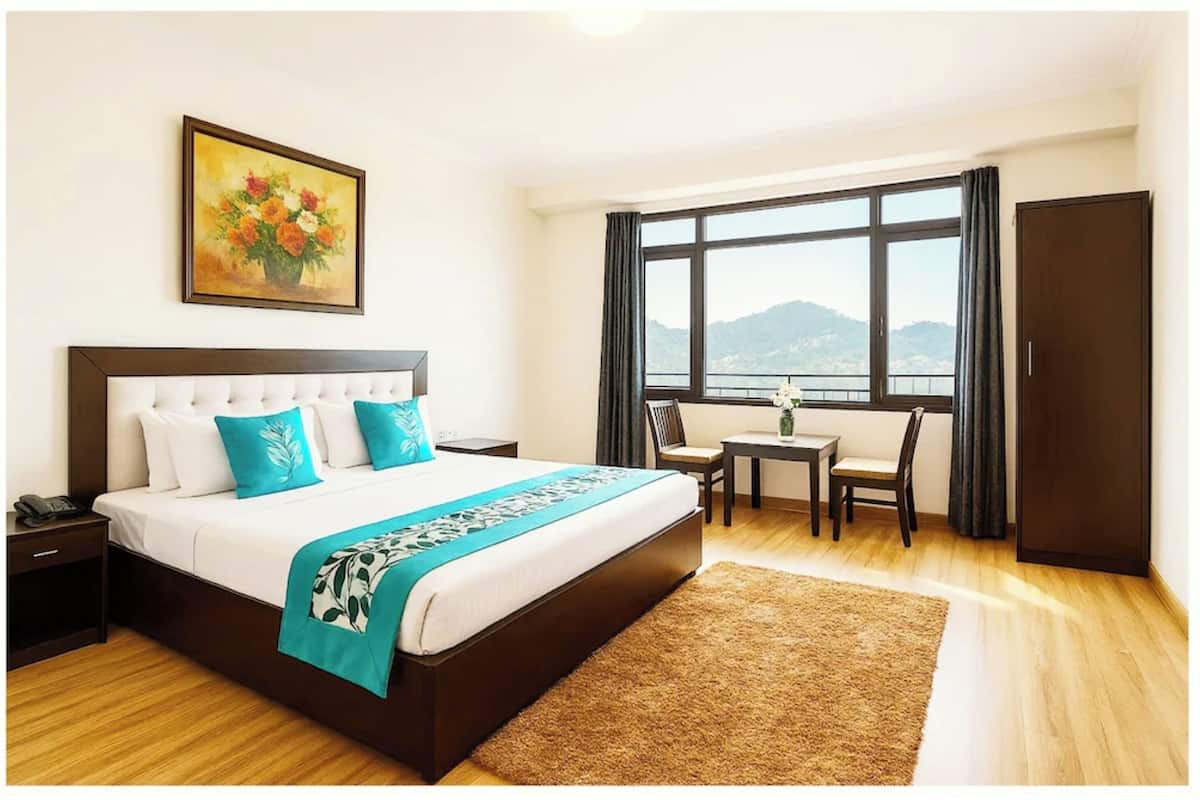 A hotel room with a bed, a desk, a chair, a window with a view, and a painting on the wall.