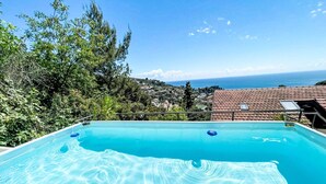 A rectangular swimming pool with clear blue water, surrounded by greenery and overlooking a coastal town. - Belle Vue by Interhome (Alassio)