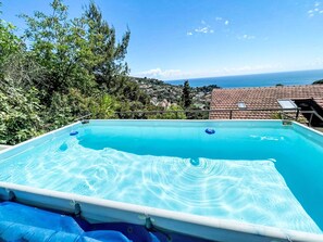 Ein rechteckiger Swimmingpool mit klarem, blauem Wasser, umgeben von Grün und mit Blick auf eine Küstenstadt.