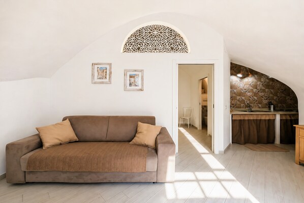 Una sala de estar moderna con un sofá, un arco decorativo en la pared y una cocina al fondo.