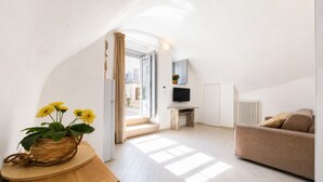 A modern living room with a sofa, a TV, a wooden table with a plant, and a view of the outside. - Casa Marosa – In the Heart of the Village (Monte Sant'Angelo)