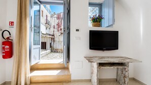 A room with a television, a fire extinguisher, a window with a view of buildings, and a door leading outside. - Casa Marosa – In the Heart of the Village (Monte Sant'Angelo)