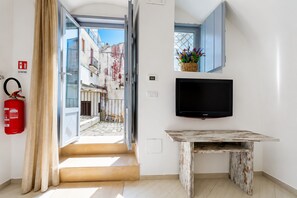 A room with a television, a fire extinguisher, a window with a view of buildings, and a door leading outside.